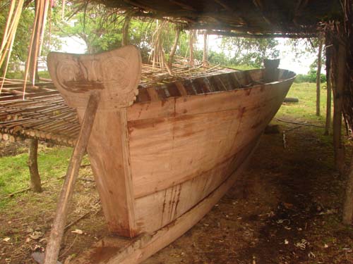 A sailing canoe being built, and stored under thatched roof