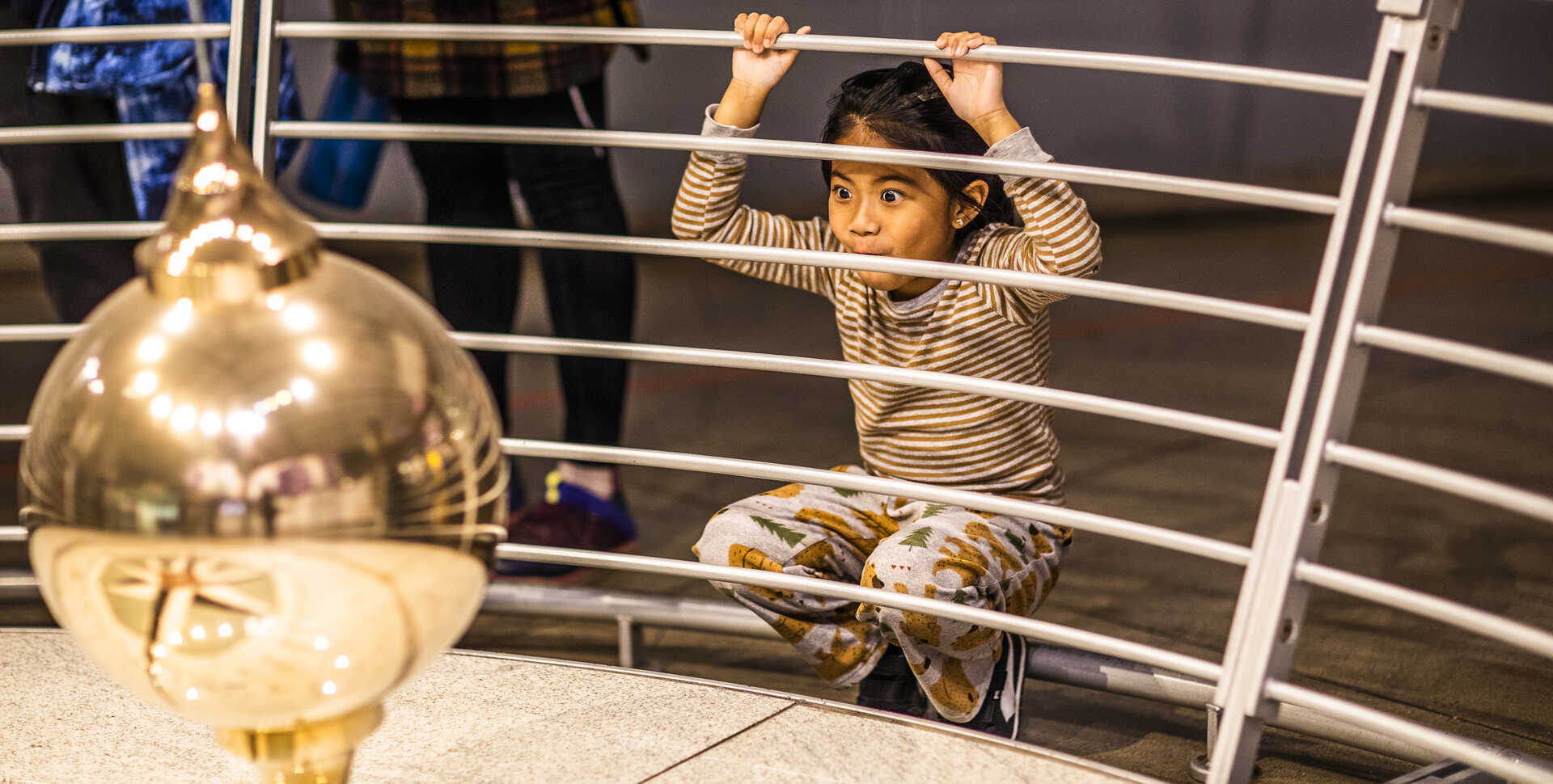 A young girl watches the Foucault pendulum knock down pins at the Academy