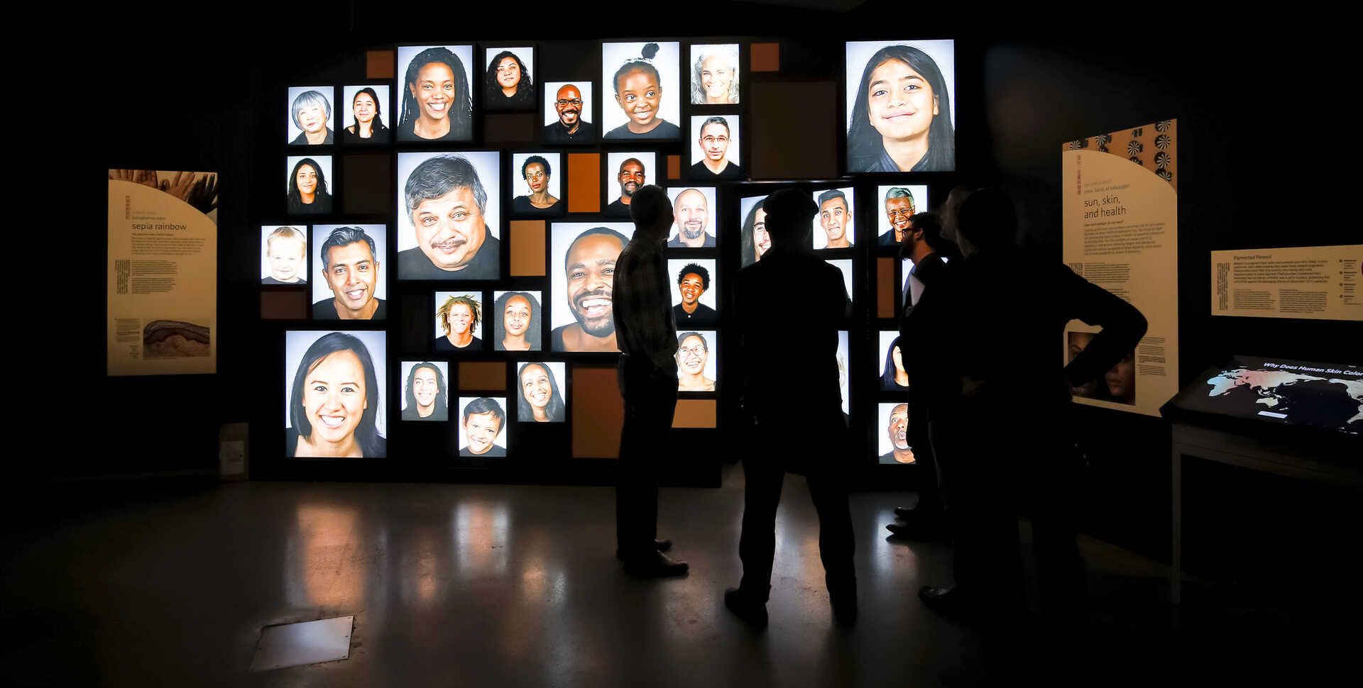 Video portrait wall from the Academy's Skin exhibit, with silhouetted guests in foreground