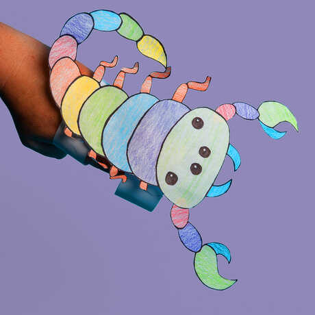 A colorful paper scorpion craft against a lavender background