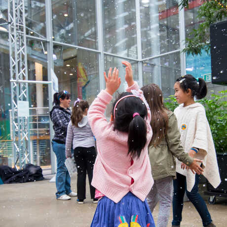 A girl reaches up to grab indoor snow flurries in the Academy Piazza