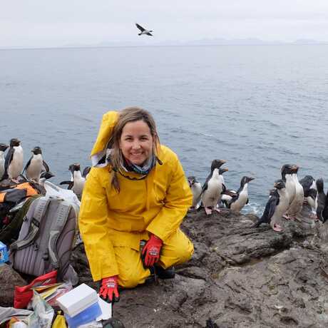 Portrait of Dr. Juliana Vianna in the field with penguins in the background