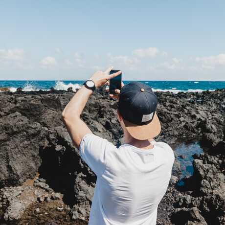 A man stands on a rocky shoreline with a cellphone