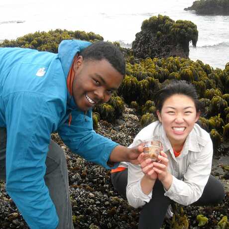 2 smiling high school students display a specimen on a rocky tidepool