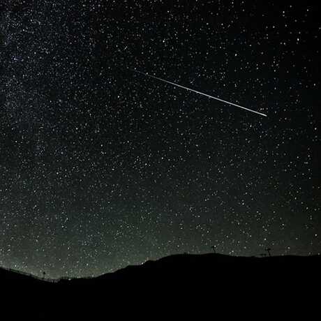 Meteor streaking over mountains through night sky