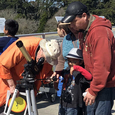 An Academy Docent helps Astronomy Day visitors observe the Sun safely.