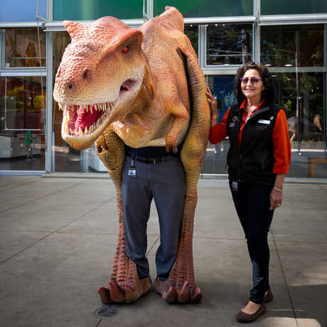 A realistic Tyrannosaurus rex costume worn by an Academy staff person, accompanied by a handler