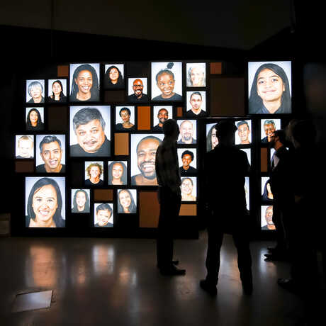 Silhouetted guests in front of a video mosaic of diverse human faces