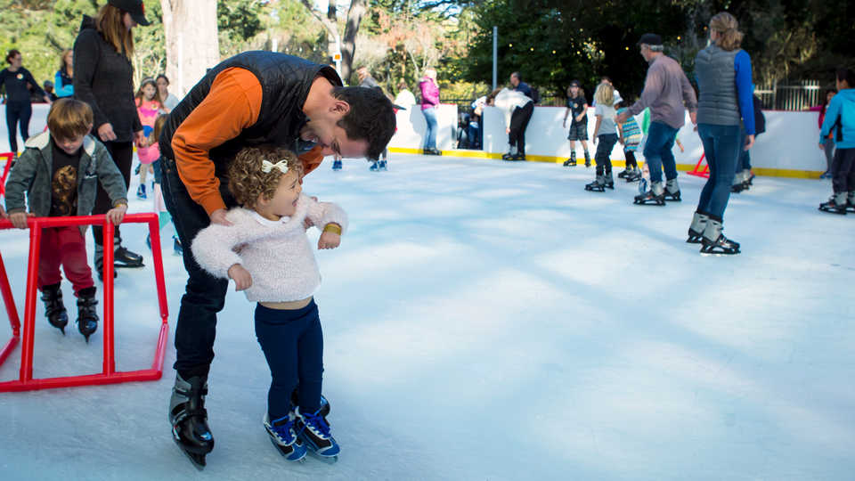 Dad teaches smiling toddler to ice skate at the Academy ice rink