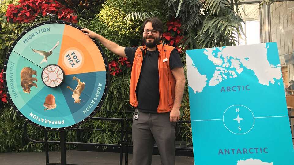 Presenter next to large game wheel and map of the arctic and antarctic 